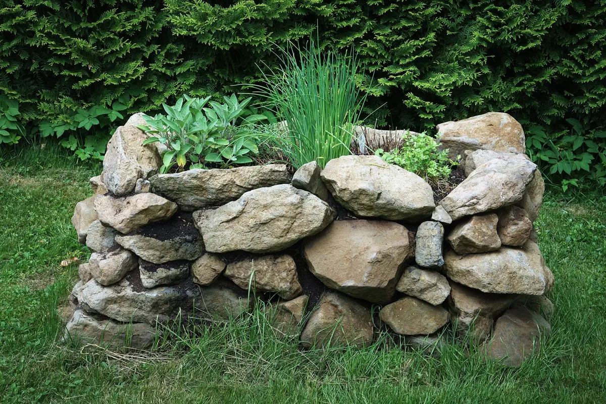 Rundes Hochbeet aus aufgeschichteten Natursteinen mit Salbei und Schnittlauch